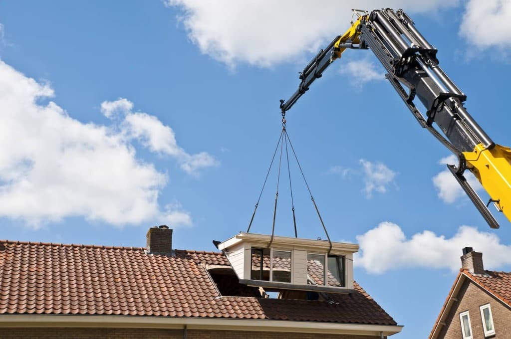Witte prefab dakkapel wordt met een hijskraan op een pannendak geplaatst